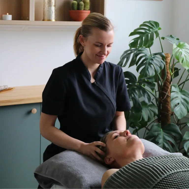 Ida, grundare av BeautyRelax sitter på en stol bakom en kund som ligger på britsen. Hon ger massage av huvudet och hårbotten.